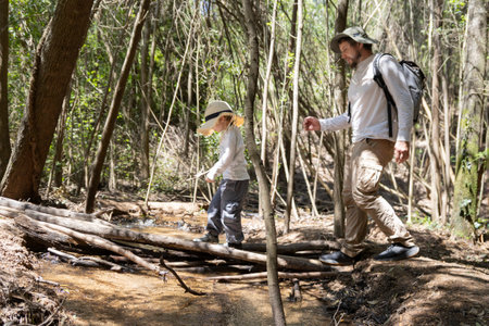 Father and son hiking and crossing a creek in forestの写真素材