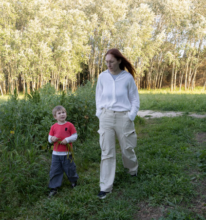 Mother and son walking through a lush green meadow by a forestの写真素材