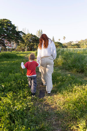 Mother and son walking through green meadow holding handsの写真素材