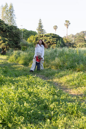 Mother carrying son walking on meadow in park during springtimeの写真素材