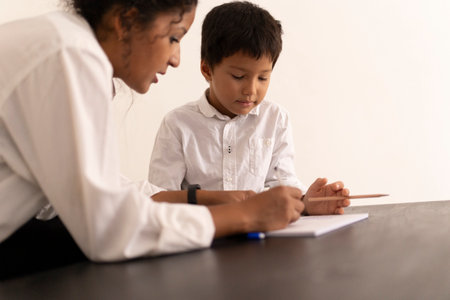 Teacher helping young pupil with writing exercise in classroomの写真素材