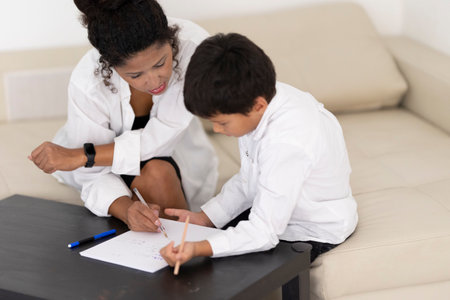 Teacher helping young boy with homework on living room tableの写真素材