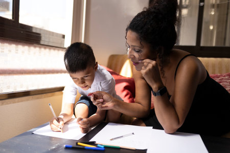 Mother helping son drawing with pencils at homeの写真素材