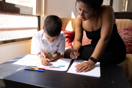 Teacher helping young student drawing with colored pencils at homeの写真素材