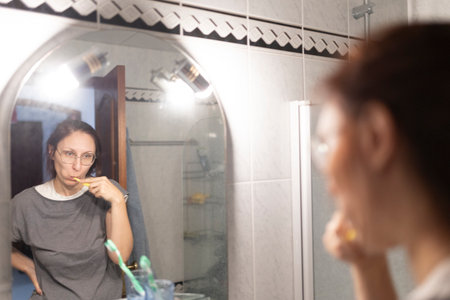 Woman brushing teeth in bathroom mirror reflecting daily oral hygiene routineの写真素材