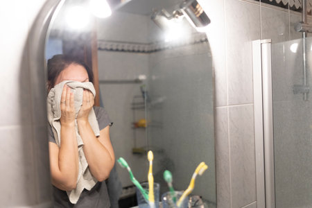 Woman drying her face with a towel after showering in the bathroomの写真素材