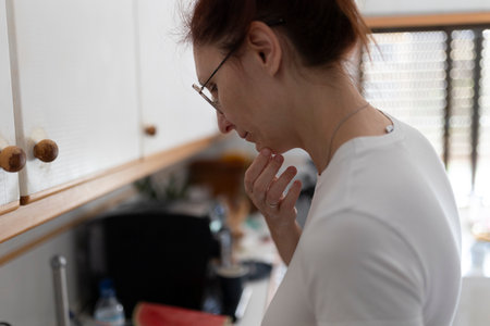 Pensive housewife contemplating in kitchen: expressing uncertainty and decision-makingの写真素材