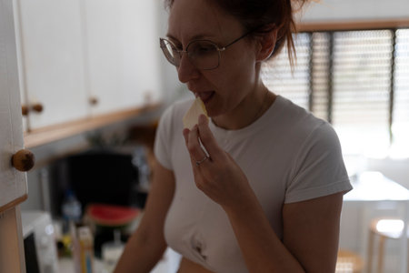 Woman enjoying slice of cheese in kitchen: healthy eating habitsの写真素材