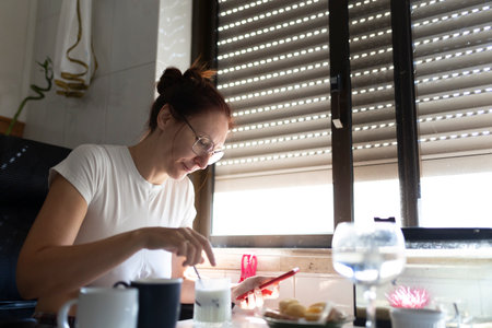 Woman enjoying breakfast and browsing smartphone at homeの写真素材