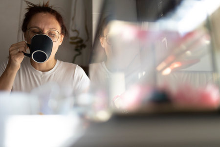 Woman drinking coffee in kitchen with reflection in glass surfaceの写真素材