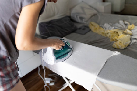 Woman ironing clothes on ironing board in bedroomの写真素材
