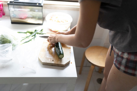Woman cutting zucchini on wooden board in kitchenの写真素材