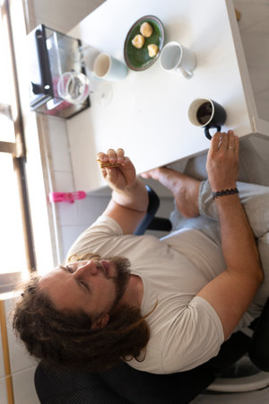 Young man relaxing at home, enjoying coffee and snackの写真素材