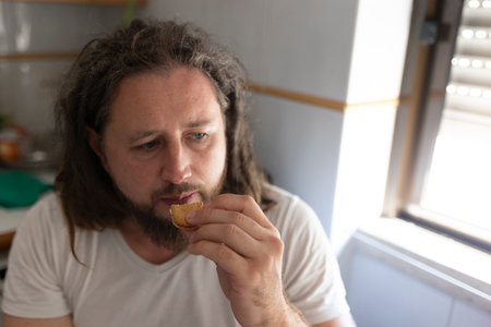 Man eating a cookie in the kitchen during daytimeの写真素材