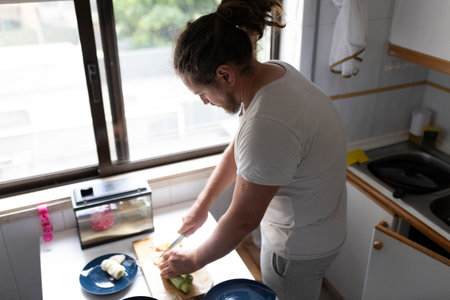 Man cutting vegetables in the kitchen near a small terrariumの写真素材