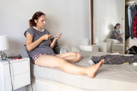 Woman doing diabetes finger prick test on bed at homeの写真素材