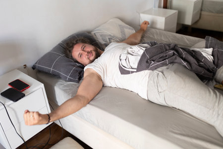 Young man waking up and stretching in bed after sleepingの写真素材