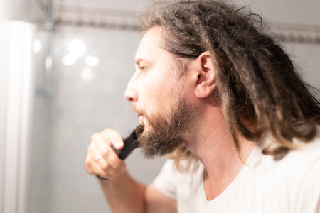 Man trimming his beard with electric razor in bathroom mirrorの写真素材