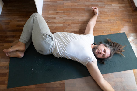 Tired man resting on yoga mat after exercising at homeの写真素材