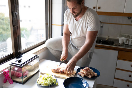 Man cutting chicken in kitchen preparing lunch with leek and terrariumの写真素材