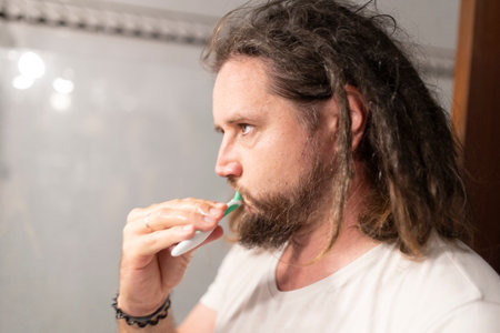 Man brushing teeth with toothbrush in bathroom mirror: oral hygiene routineの写真素材