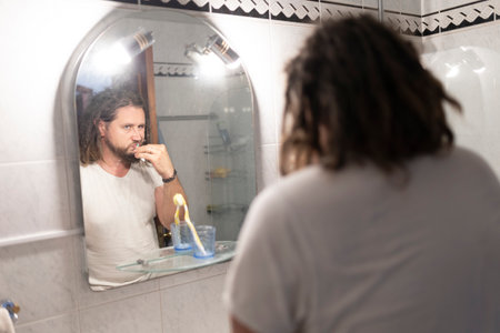 Man brushing teeth in bathroom mirror reflecting daily routineの写真素材
