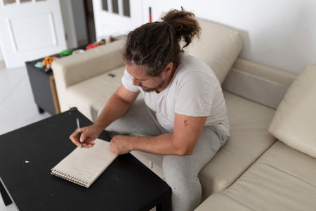 Man writing notes on notepad while sitting on sofa at homeの写真素材