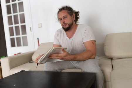 Man drawing on notepad while sitting on sofa in living roomの写真素材