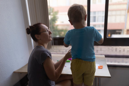 Mother and son playing with modeling clay near windowの写真素材