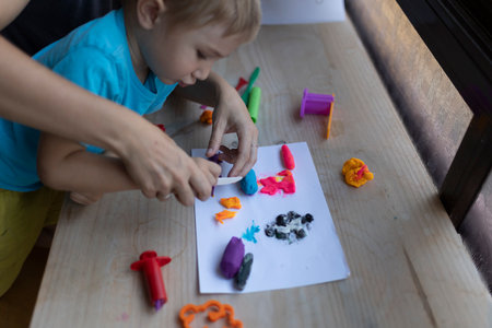 Child and kindergarten teacher cutting colorful clay with plastic knife on tableの写真素材