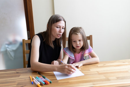 Mother helping daughter with homework at home: homeschooling during pandemicの写真素材