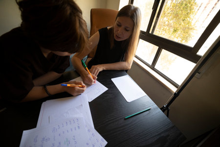Teacher helping student with homework, writing on paper at home