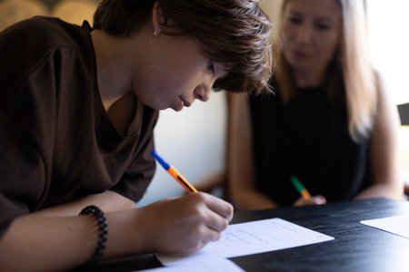 Teenage student writing notes during class with teacher assisting