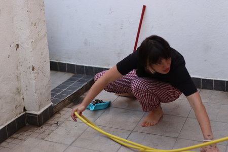 Young woman cleaning patio with yellow hose and dustpanの写真素材