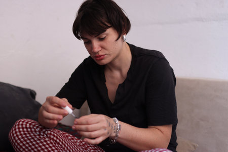 Young woman applying nail polish on sofa at homeの写真素材