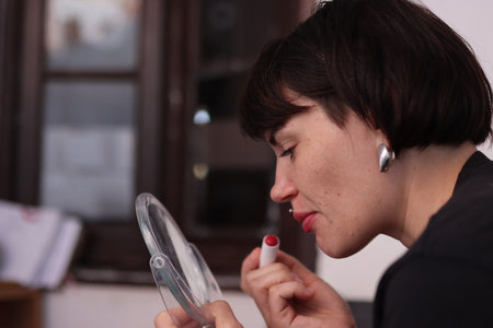 Woman applying red lipstick while looking in a mirrorの写真素材
