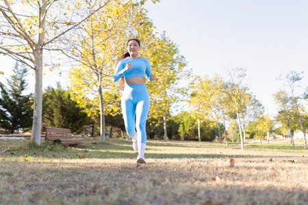 Young sportswoman running in a park during a sunny autumn dayの写真素材