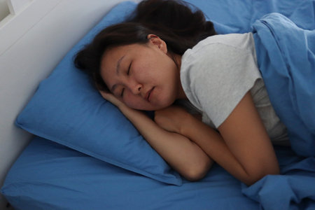 Young asian woman sleeping peacefully in bed on blue sheetsの写真素材