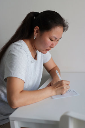 Asian woman writing notes at home office deskの写真素材