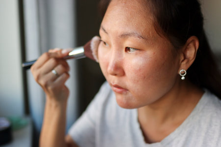 Asian woman applying makeup powder with brush: beauty routine at homeの写真素材