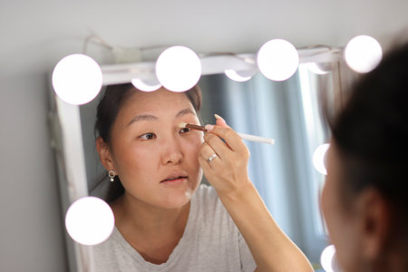 Woman applying makeup in front of mirror with lightsの写真素材