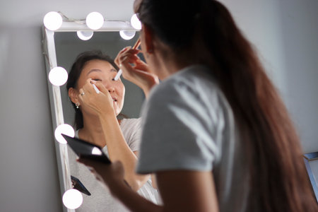 Woman applying makeup in front of mirror with lightsの写真素材