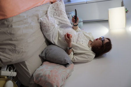 Pregnant woman relaxing on bed watching tv and eating appleの写真素材