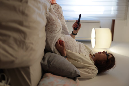 Pregnant woman relaxing on bed, watching tv and holding remote controlの写真素材