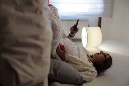 Pregnant woman relaxing on bed watching tv and holding remote controlの写真素材