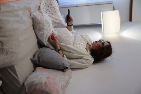 Pregnant woman relaxing on bed, watching tv and eating appleの写真素材