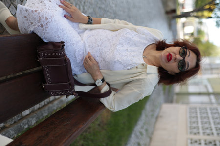Elegant woman relaxing on bench in city parkの写真素材