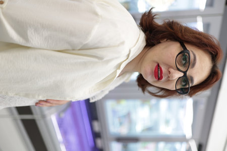 Woman wearing glasses and red lipstick looking down in supermarket refrigerator aisleの写真素材