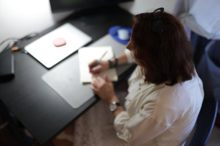 Woman writing notes at home office desk working remotelyの写真素材