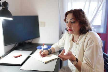 Businesswoman taking notes and gesturing while working from homeの写真素材